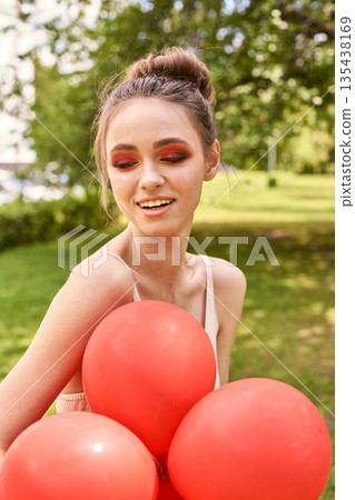 Young caucasian female with red balloons smiling outdoors in sunny park setting Young caucasian female with red balloons smiling outdoors in sunny park setting 135438169