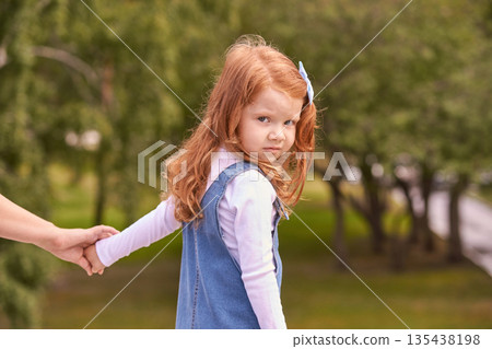 Young caucasian female child with red hair holding hand outdoors in park Young caucasian female child with red hair holding hand outdoors in park 135438198