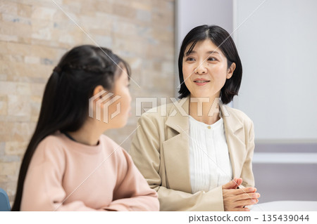 A mother in a suit talking to an elementary school girl A mother in a suit talking to an elementary school girl 135439044