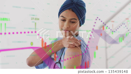 Touching bandage on arm, nurse in scrubs and turban in studio with stethoscope and financial chart 135439148