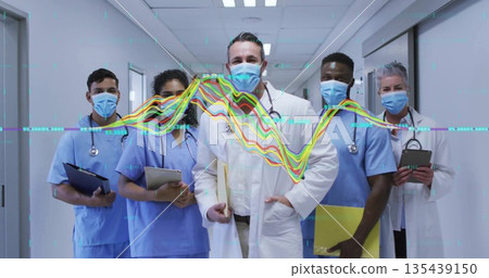 Standing team in uniforms reviewing data in hospital hallway, with stethoscopes waveform graphic 135439150