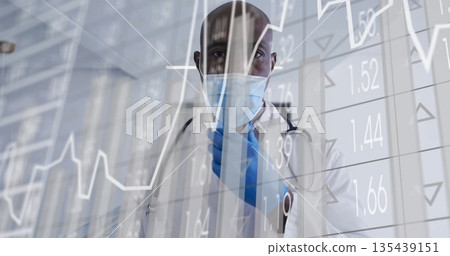 Standing male doctor wearing lab coat surgical mask behind data panel at clinic, with stethoscope 135439151