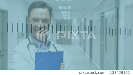 Holding blue clipboard and stethoscope, doctor wearing white coat standing in hospital corridor Holding blue clipboard and stethoscope, doctor wearing white coat standing in hospital corridor 135439163