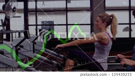 Rowing female athlete pulling handle on rower at gym, with performance data overlays, copy space 135439255