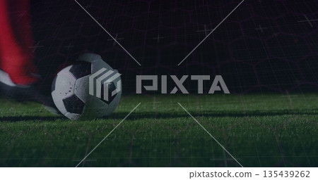 Resting classic soccer ball beneath red sock and black cleat on night pitch, with digital grid Resting classic soccer ball beneath red sock and black cleat on night pitch, with digital grid 135439262