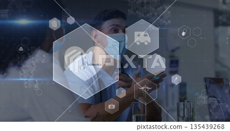 Gesturing masked clinician in scrubs explaining data in clinic with laptop, glasses and overlays Gesturing masked clinician in scrubs explaining data in clinic with laptop, glasses and overlays 135439268