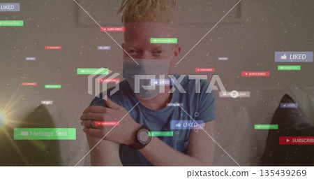 Man wearing gray mask, blue tee rubbing arm on gray couch at home, with smartwatch, icons 135439269