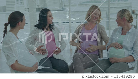 Chatting women in maternitywear with baby bumps in prenatal class, white chairs and skyline windows 135439290