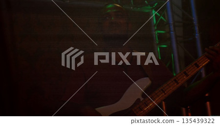 Performing adult male musician playing bass guitar on dark stage with green LED and red glow Performing adult male musician playing bass guitar on dark stage with green LED and red glow 135439322