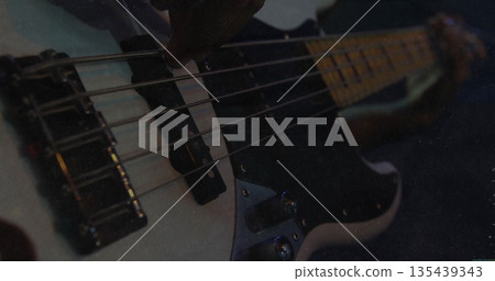 Plucking white electric bass guitar strings in dimly lit studio, over pickups and fretboard Plucking white electric bass guitar strings in dimly lit studio, over pickups and fretboard 135439343