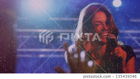 Reaching sleeveless singer singing into microphone on stage amid confetti under lights, copy space Reaching sleeveless singer singing into microphone on stage amid confetti under lights, copy space 135439346
