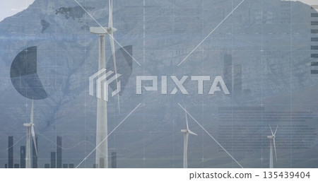 Spinning central white wind turbine on grassy field at mountain base, with three-blade rotor 135439404