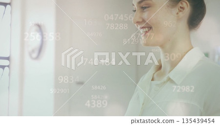 Smiling professional woman viewing floating numeric overlays in office workspace, with wall clock Smiling professional woman viewing floating numeric overlays in office workspace, with wall clock 135439454