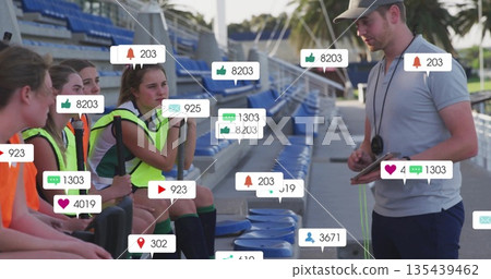 Male coach holding tablet coaching players wearing neon vests on bleachers, with soccer balls 135439462