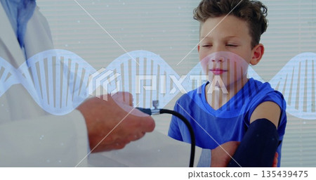 Measuring boy's blood pressure while doctor inflating cuff in exam room with DNA helix, copy space 135439475