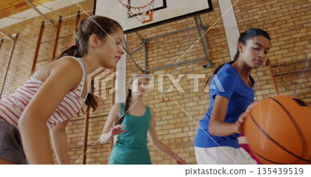 Dribbling girl in blue t-shirt and shorts on school gym floor with basketball hoop, copy space 135439519