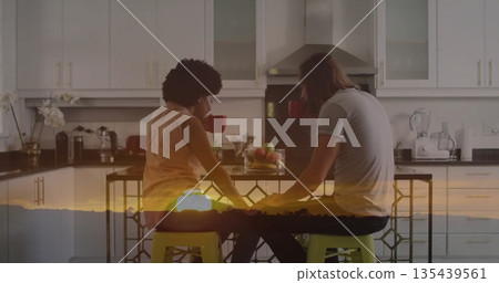 Chatting couple sitting at kitchen island with clear glass bowl of apples, holding red coffee mugs Chatting couple sitting at kitchen island with clear glass bowl of apples, holding red coffee mugs 135439561