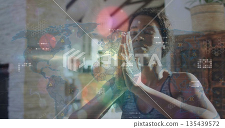 Woman wearing tank top meditating in yoga studio against white brick wall, with digital overlay Woman wearing tank top meditating in yoga studio against white brick wall, with digital overlay 135439572
