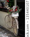 Vintage bicycle decorated with Christmas greenery and ornaments against a dark wall 135440107