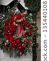 Festive red and green Christmas wreath with ornaments and ribbons displayed on a wall 135440108