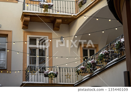 Cozy courtyard with string lights and flower pots during winter season with snow on the ground Cozy courtyard with string lights and flower pots during winter season with snow on the ground 135440109