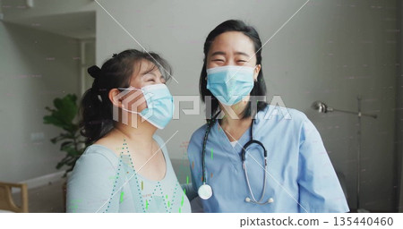 Smiling doctor in scrubs and patient standing in exam room, showing stethoscope and surgical masks Smiling doctor in scrubs and patient standing in exam room, showing stethoscope and surgical masks 135440460