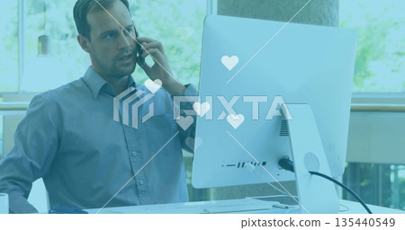 Talking worker wearing blue shirt holding smartphone looking at computer at office, copy space 135440549
