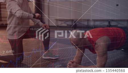 Performing plank exercise man on rubber mat at gym with kneeling trainer, showing financial charts Performing plank exercise man on rubber mat at gym with kneeling trainer, showing financial charts 135440568