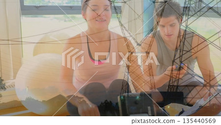 Rowing partners wearing gymwear on rowing machines in home gym, with exercise ball and water bottle Rowing partners wearing gymwear on rowing machines in home gym, with exercise ball and water bottle 135440569