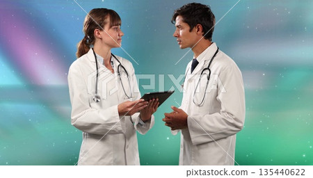 Two doctors wearing white coats holding tablet and discussing in studio, with two stethoscopes 135440622