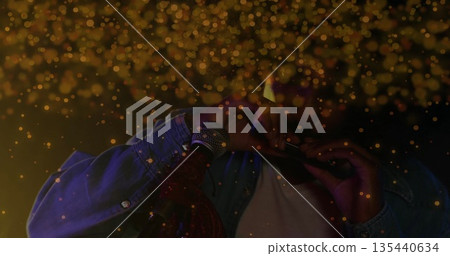 Playing musician in denim jacket blowing harmonica at microphone stand on dark stage, golden bokeh 135440634