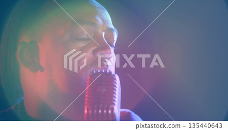Singing male singer wearing dark shirt, holding retro microphone on stage with colored spotlights 135440643