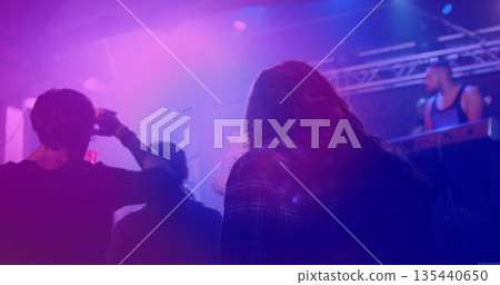 Watching long-haired man wearing plaid shirt shading eyes at music venue, with keyboard rig haze 135440650