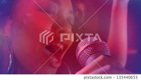 Singing singer wearing stage makeup on club stage, with wired microphone, colored lights and haze Singing singer wearing stage makeup on club stage, with wired microphone, colored lights and haze 135440653