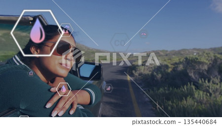 Leaning on car door, woman wearing shades gazing on road with AR water-CO icons, copy space 135440684