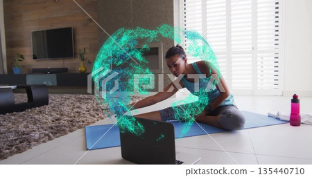 Performing hamstring stretch Asian woman facing laptop on yoga mat at home, with holographic globe Performing hamstring stretch Asian woman facing laptop on yoga mat at home, with holographic globe 135440710