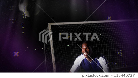 Crouching male goalkeeper in blue white jersey at night soccer field, with soccer ball, copy space Crouching male goalkeeper in blue white jersey at night soccer field, with soccer ball, copy space 135440727
