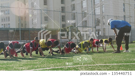 Youth soccer players wearing bibs performing push-ups on turf, with coach guiding and orange cones 135440751