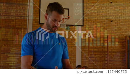 Coach wearing blue shirt guiding trainee in gym, with basketball hoop, climbing bars and bench 135440755