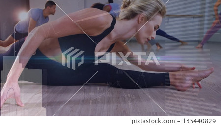 Stretching adult woman in black activewear leaning toward right leg in studio, with ballet barre Stretching adult woman in black activewear leaning toward right leg in studio, with ballet barre 135440829