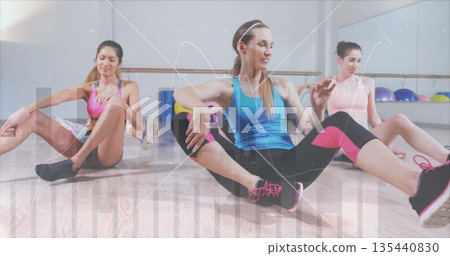 Stretching three women wearing athletic wear seated on studio floor, with barre and exercise balls Stretching three women wearing athletic wear seated on studio floor, with barre and exercise balls 135440830