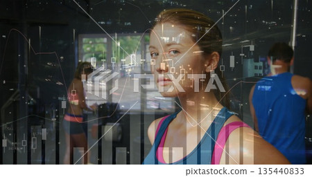 Standing woman in blue tank top exercising at gym, with treadmill, weights and financial charts 135440833