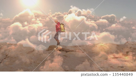Standing hiker wearing bright red jacket and neon green backpack on mountain ledge, above clouds 135440849