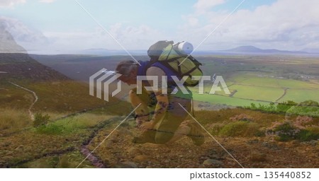 Kneeling adult hiker tying boot laces on mountain trail, with hiking backpack and valley view 135440852