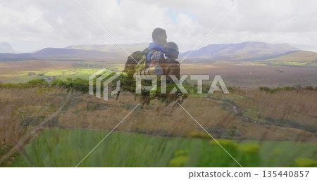 Standing couple of hikers overlooking valley from grassy hillside, with backpacks and rolled mat Standing couple of hikers overlooking valley from grassy hillside, with backpacks and rolled mat 135440857