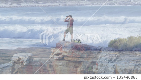 Scanning man in red shirt and khaki shorts using binoculars on coastal rocky outcrop, with backpack Scanning man in red shirt and khaki shorts using binoculars on coastal rocky outcrop, with backpack 135440863