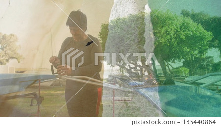 Adjusting senior fisher tightening fishing reel on metal rod rack by lake, with lounge chairs Adjusting senior fisher tightening fishing reel on metal rod rack by lake, with lounge chairs 135440864