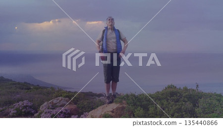 Standing hiker surveying ocean on rocky hilltop, with backpack hiking boots fingerless gloves 135440866