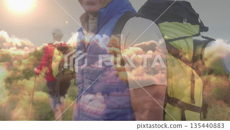 Standing man in blue vest carrying backpack on grassy hillside, trekking pole visible, sky overlay Standing man in blue vest carrying backpack on grassy hillside, trekking pole visible, sky overlay 135440883