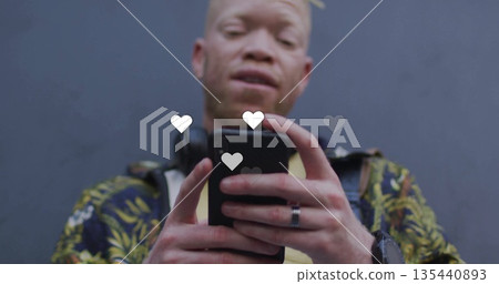 Man in floral jacket over ear headphones holding smartphone at gray wall, with floating heart icons Man in floral jacket over ear headphones holding smartphone at gray wall, with floating heart icons 135440893